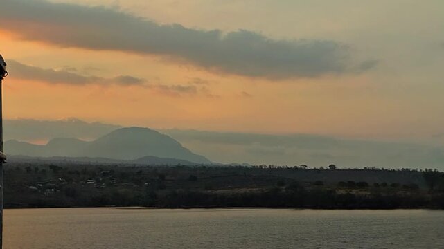 Scenic panoramic view of tropical mountain range and calm sea during golden hour sunset. Tranquil natural landscape footage suitable for travel b-roll and relaxation background video.
