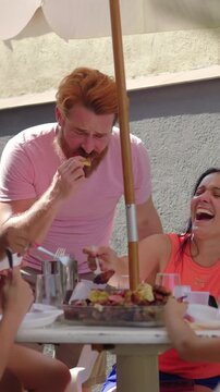 Joyful friends enjoying food and conversation outdoors under patio umbrella