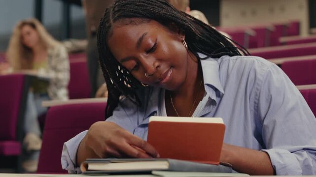 Focused black female student writing in lecture hall