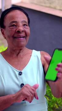 Elderly African American woman presenting green screen smartphone outdoors, display mockup