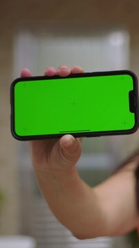 Hand holding smartphone with horizontal green screen close up, landscape mobile mockup