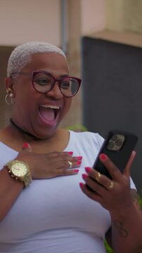 Joyful African American woman reacting to smartphone outdoors, excited surprise