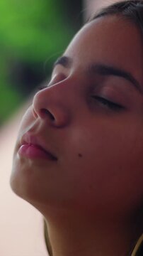 Peaceful young girl with brown hair closing eyes against wall outdoors, relaxed mood