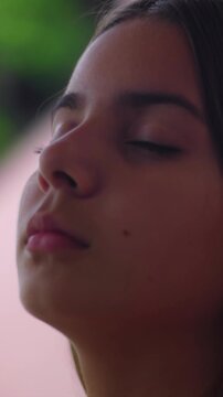 Relaxed young girl with brown hair closing eyes outdoors, experiencing inner peace