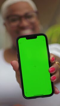 Smiling African American woman holding green screen smartphone towards camera, app display mockup