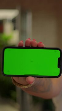 Smiling African American woman presenting horizontal smartphone green screen outdoors