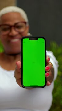Smiling African American woman presenting vertical green screen smartphone outdoors, app display mockup