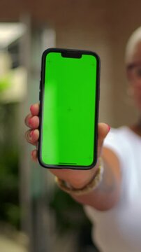 Smiling African American woman presenting vertical smartphone green screen outdoors