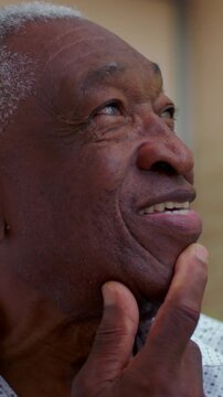 Smiling elderly African American man thinking with hand on chin outdoors, thoughtful senior portrait