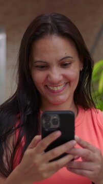 Smiling woman looking at smartphone outdoors, cheerful mobile screen interaction
