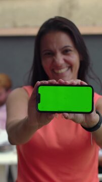 Smiling woman holding smartphone green screen towards camera outdoors, display mockup
