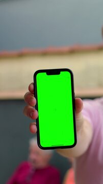 Surprised man showing smartphone with green screen outdoors, unexpected app reveal