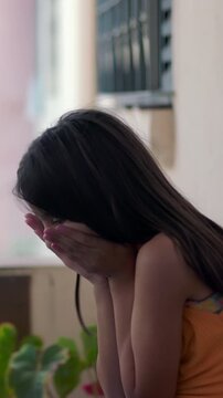 Traumatized young child sitting on outdoor floor with hands covering face in distress