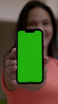 Woman holding smartphone with vertical green screen towards camera, mobile mockup