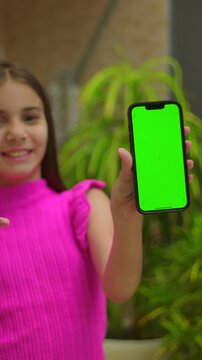 Young girl showing vertical smartphone green screen outdoors, smiling child mobile mockup