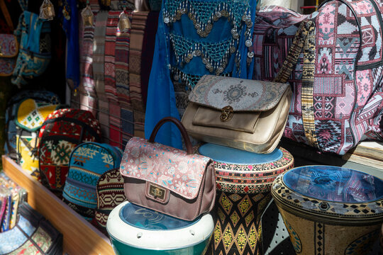 Colorful embroidered handbags, patterned backpacks and decorated goblet drums displayed outside souvenir shop, featuring intricate geometric textile designs.
