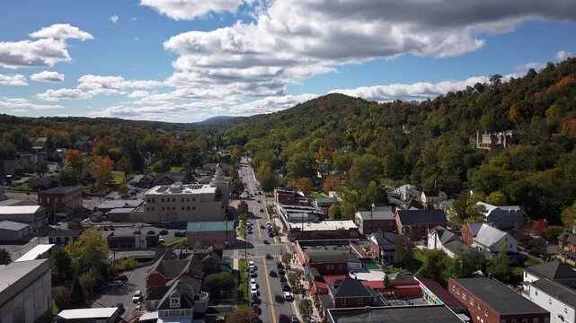 Cars and clouds rush past above Bath in Berkeley Springs, West Virginia, beneath colorful autumn hills on a beautiful day.