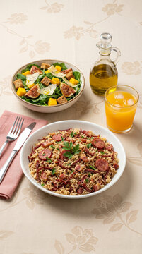 Rice with sausage, bacon, and dried beef, served with a leafy green salad featuring figs and mango, and a refreshing natural orange juice - Arroz Carreteiro 