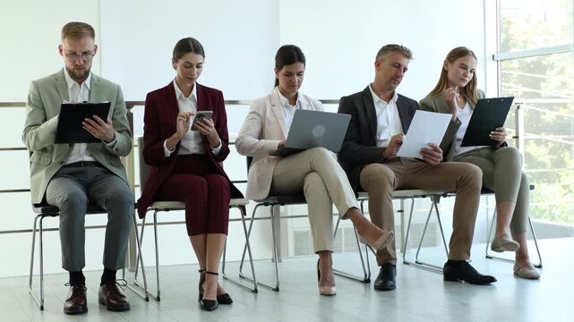 Group of people waiting in queue for job interview on chairs indoors