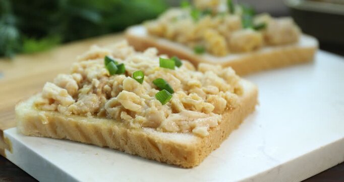 Adding chopped green onion to sandwich with cod liver on board, closeup