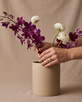 Hands arranging purple orchids and white ranunculus in a vase  