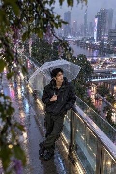 Young man holding transparent umbrella standing on city bridge during
