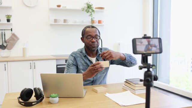 An African American creator presents a smartwatch and its small box at a desk, recording a product demonstration beside a laptop and headphones