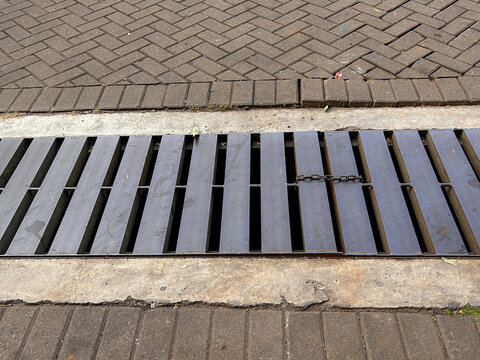 a long metal trench drain grate cover installed alongside herringbone brick paving.