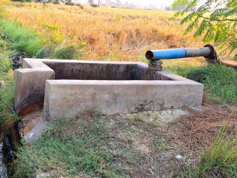 Concrete water tank with blue pipe in dry grassy field