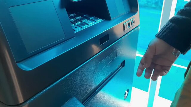 Woman hand withdraws cash from ATM machine. Blue light illuminates metallic surface. User interacts with banking machine. Modern payment solution in public space. Urban setting for daily transactions