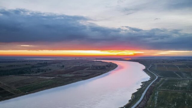 Aerial dawn time-lapse of winding Yellow River, sunrise gilding meandering channels, sorghum fields and loess banks, Baotou city, Inner Mongolia, China.