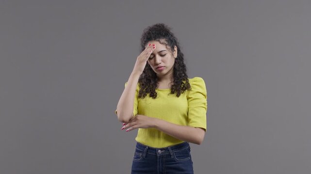 A South Asian woman closes her eyes, touches her forehead and then opens both palms with a weary, exasperated expression.
