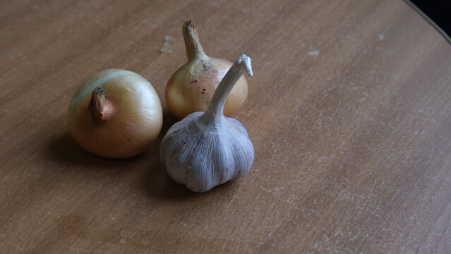 Whole raw garlic bulb and two yellow onions placed on a rustic wooden surface. Natural organic ingredients for cooking and healthy culinary recipes.