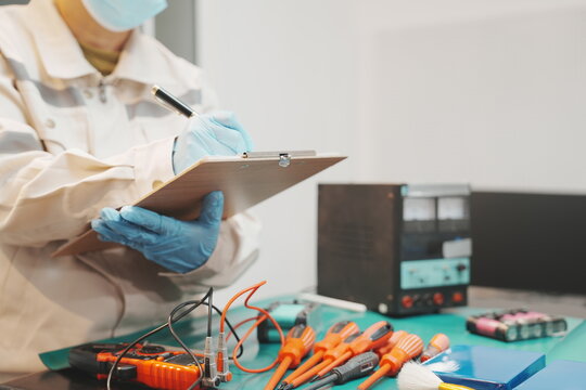 Engineers wearing protective gear conduct testing and assembly of lithium battery packs using electronic measurement equipment, power inverters, and testing tools inside a modern laboratory workshop.