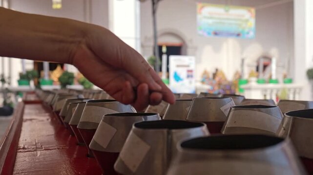 Hand dropping coins into alms bowls in a Thai temple