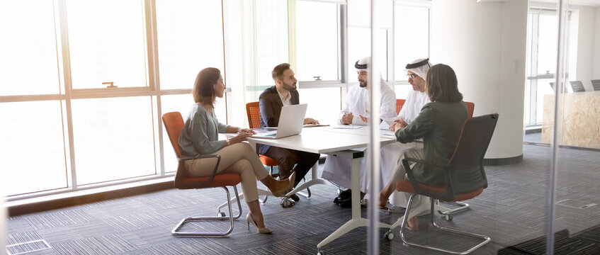 Multicultural corporate team sit at conference table, negotiating, discussing business ideas, developing strategy, reviewing international project plans, making decision in office meeting room, banner