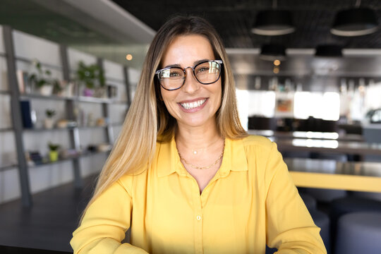 Head shot portrait beautiful smiling professional woman looks at camera seated at desk in modern coworking office, web cam view. Profile picture of video conference participant, virtual meeting event