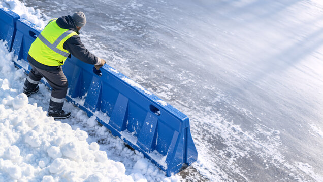 High angle view of municipal worker setting up blue road barrier in snow. Worker placing traffic barricade on icy road in winter