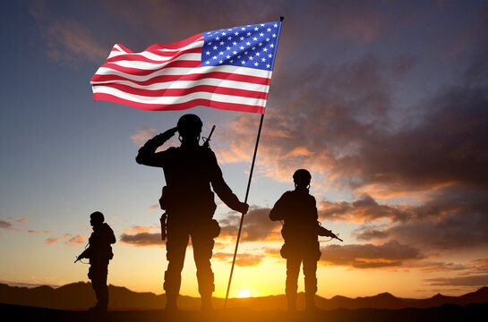 Silhouettes of a soldiers with USA flag against the sunset. Veterans Day concept