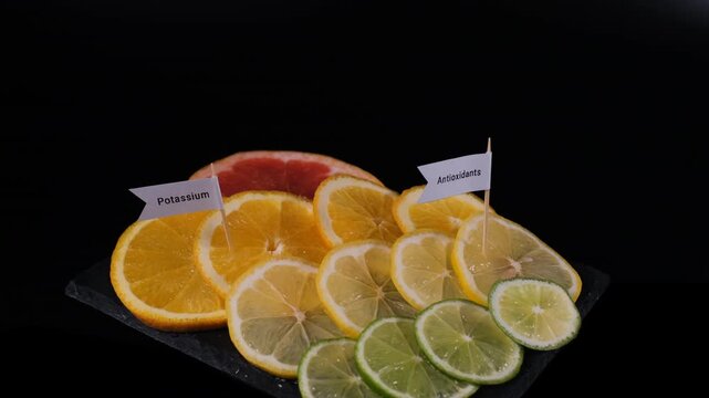 A male hand inserts potassium, vitamin C, citric acid and antioxidant markers into citrus slices on black slate. Healthy fruit concept