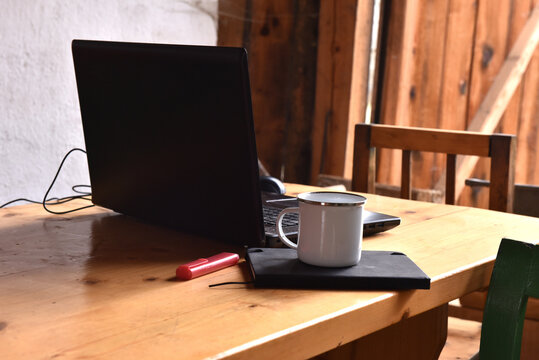 Laptop with enamel mug and notebook on a rustic wooden table
