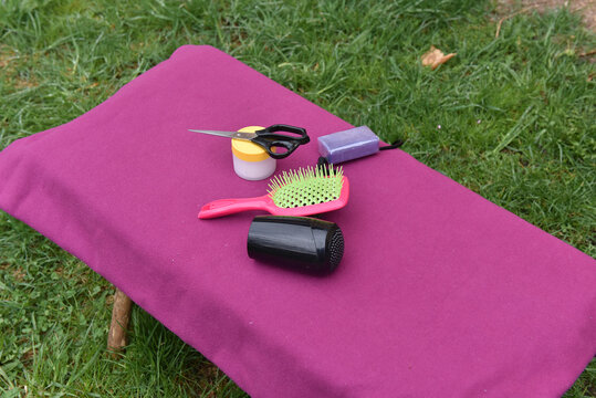 Hair styling kit with pink brush, hair dryer and accessories on a purple outdoor bench