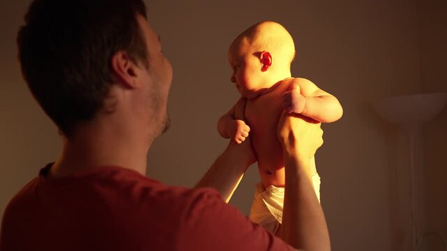 Young caucasian father affectionately holding his adorable newborn baby up in the golden light of a warm sunset, creating a beautiful silhouette of their loving bond and family connection