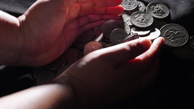 Handful of money, hands holding silver coins over pile of coins on black fabric, wealth and savings