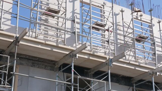 Close-up of metal scaffolding on concrete walls and window openings with rebar on top against a blue sky, French Riviera, France.