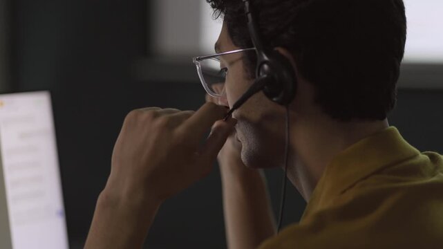 Help Desk Technician communicates through headset while gesturing near screen, guiding client through professional technical solution, illustrating practical office service interaction.