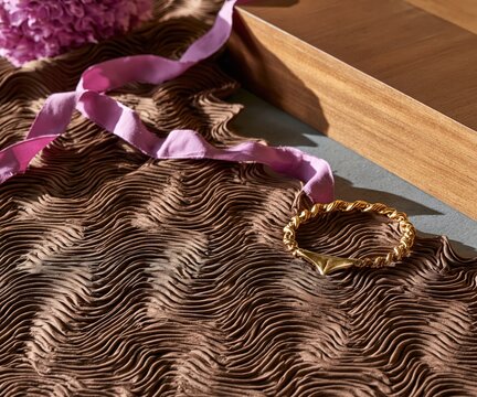 A textured fabric displays a delicate ribbon and a luxurious bracelet.