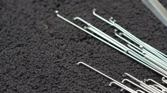 Stainless steel bicycle spokes being laid one by one on a dark cloth, close up. Parts for building a bicycle wheel by hand, shallow depth of field, real time 4K.