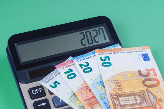 Black electronic calculator showing 2027 number on screen with euro banknotes over green background. Financial planning, 2027 business budget and tax forecasting concept.