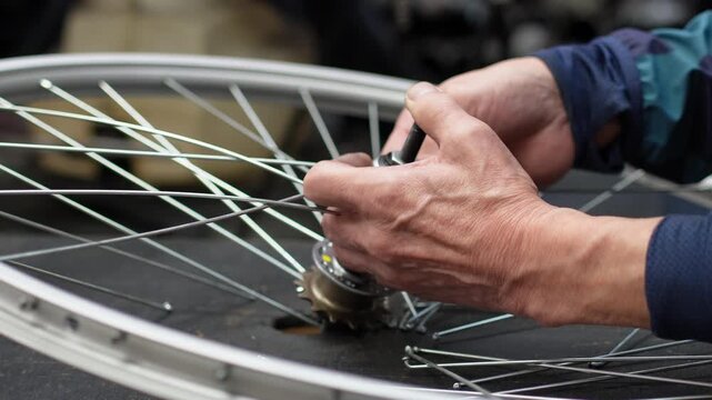 Close up of hands lacing spokes into a bicycle hub, crossing them over the flange on a dark workbench. Building a wheel by hand in a workshop, shallow depth of field, real time 4K.